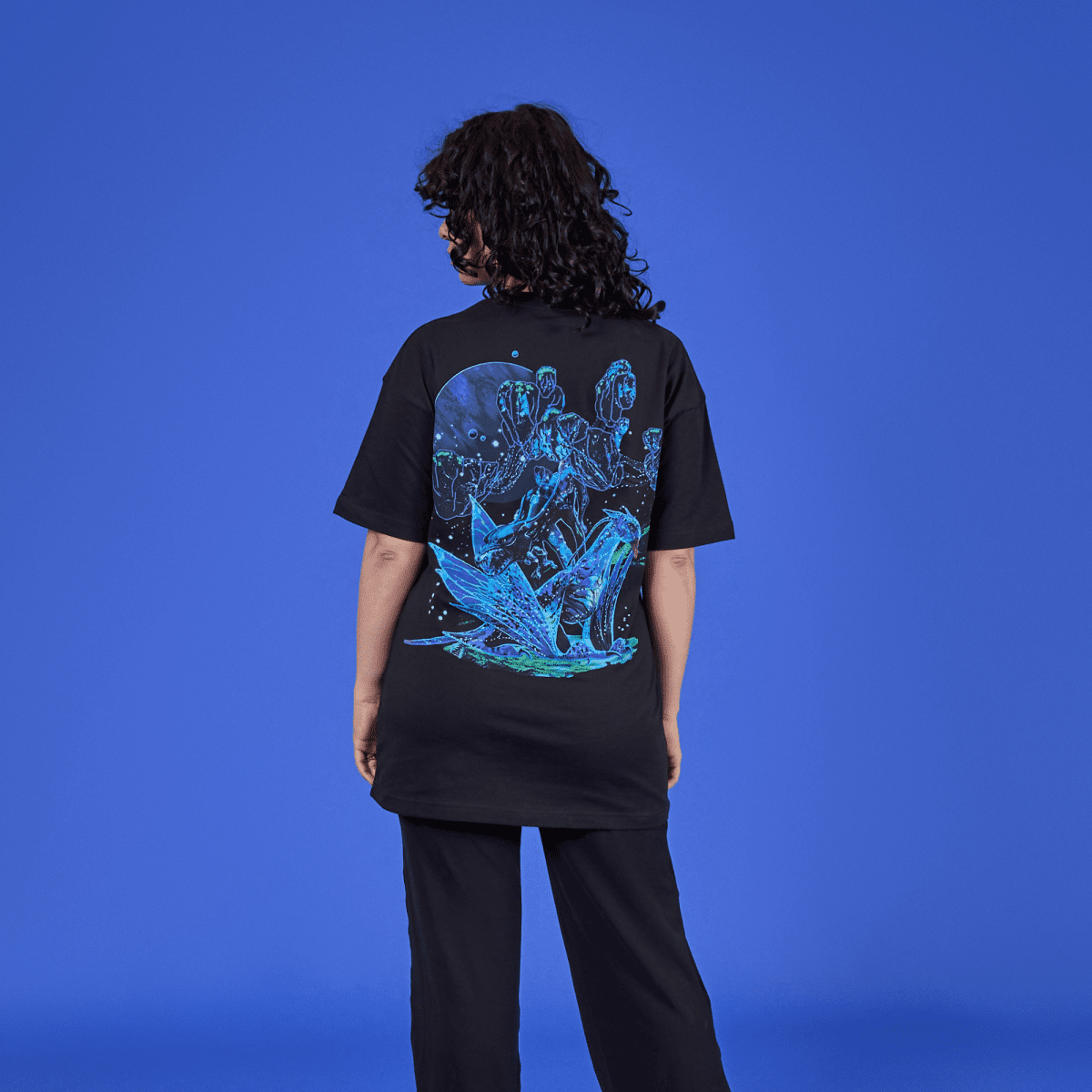 Person wearing a black t-shirt with a colorful graphic design on the back against a blue background