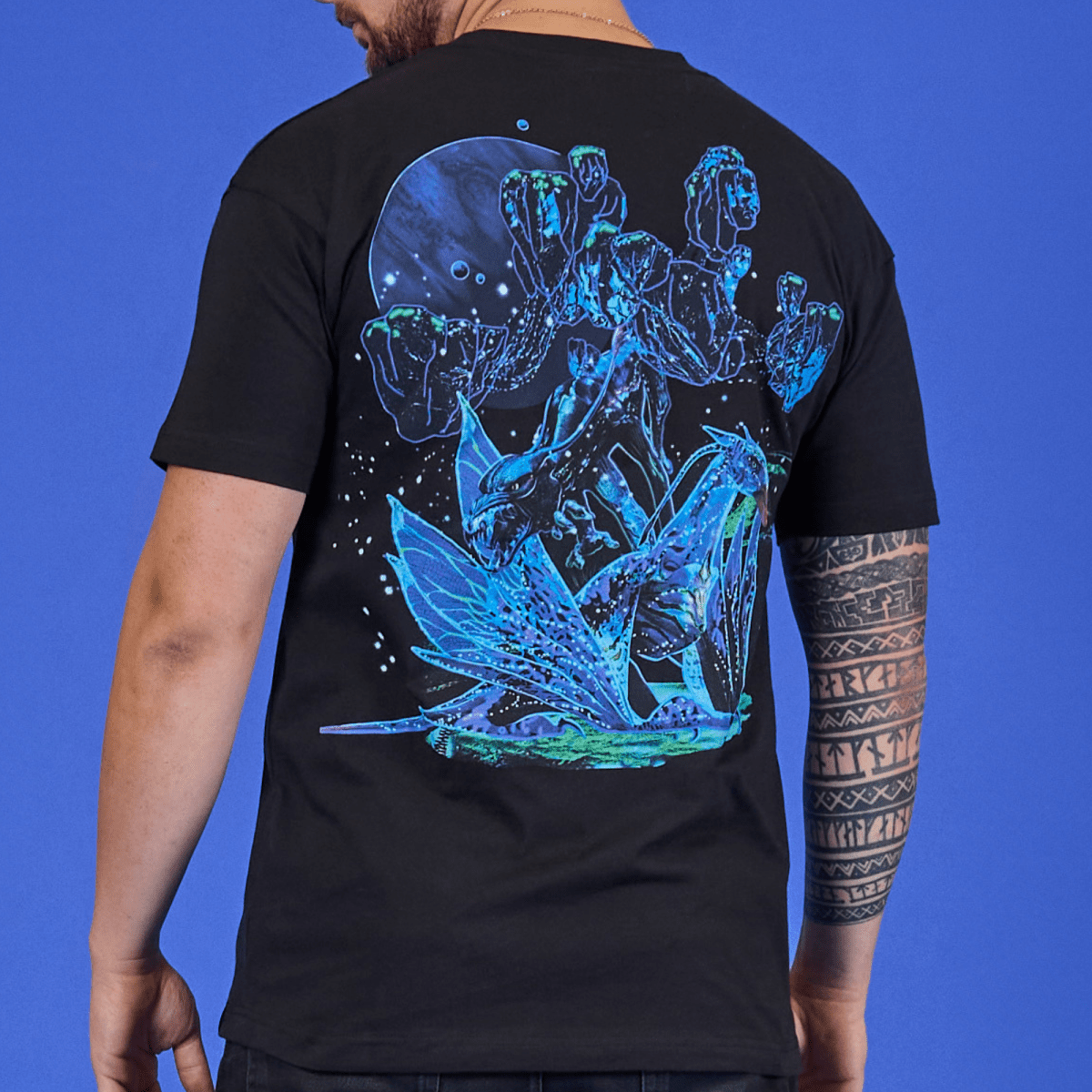 Person wearing a black t-shirt with a blue and green alien design on the back against a blue background