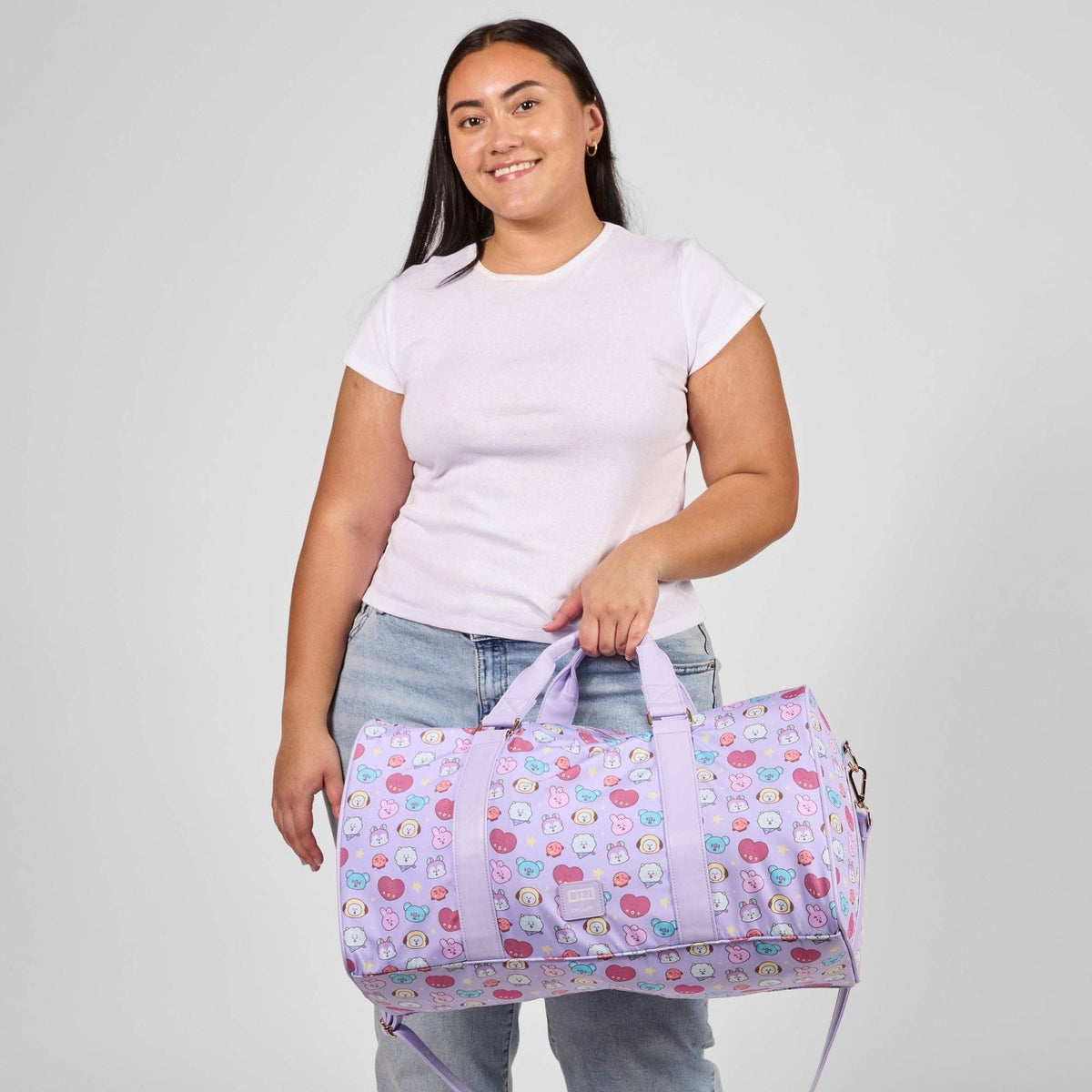 Person holding a purple duffel bag with cartoon character pattern against a plain background