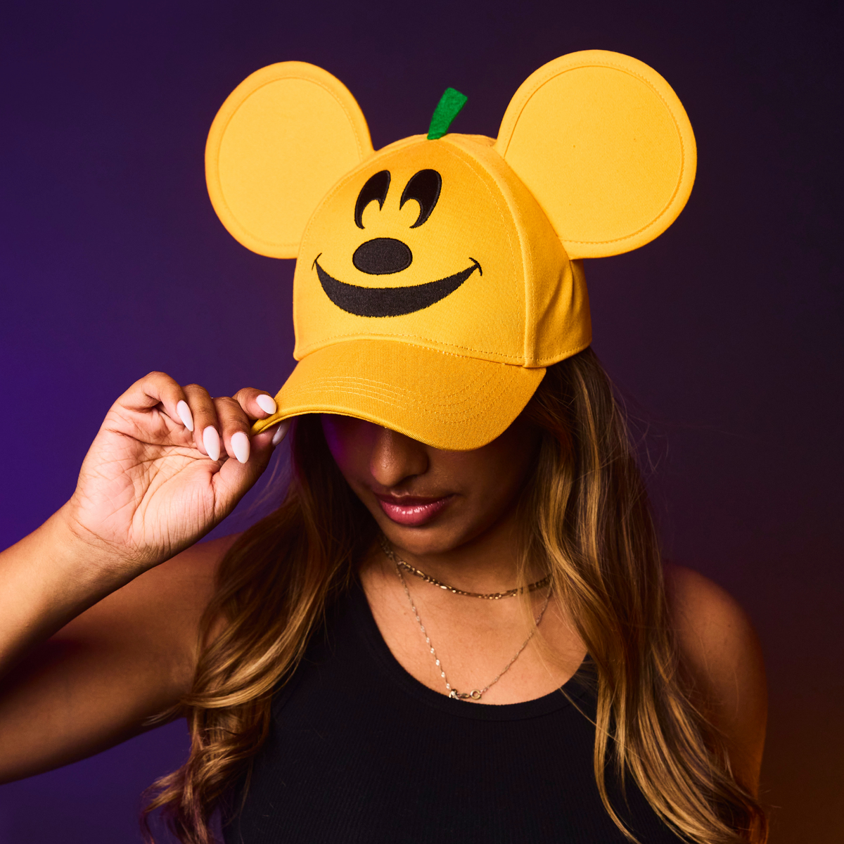 Person wearing an orange cap with mouse ears and a smiley face design against a dark background