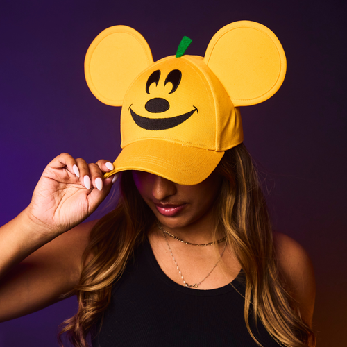 Person wearing an orange cap with mouse ears and a smiley face design against a dark background