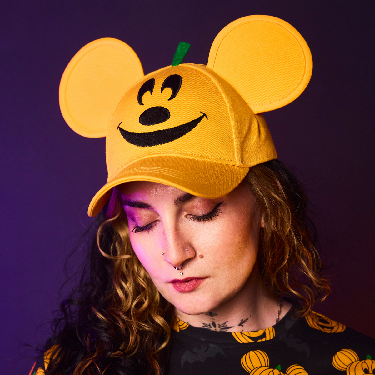 Person wearing an orange cap with a pumpkin design against a purple background