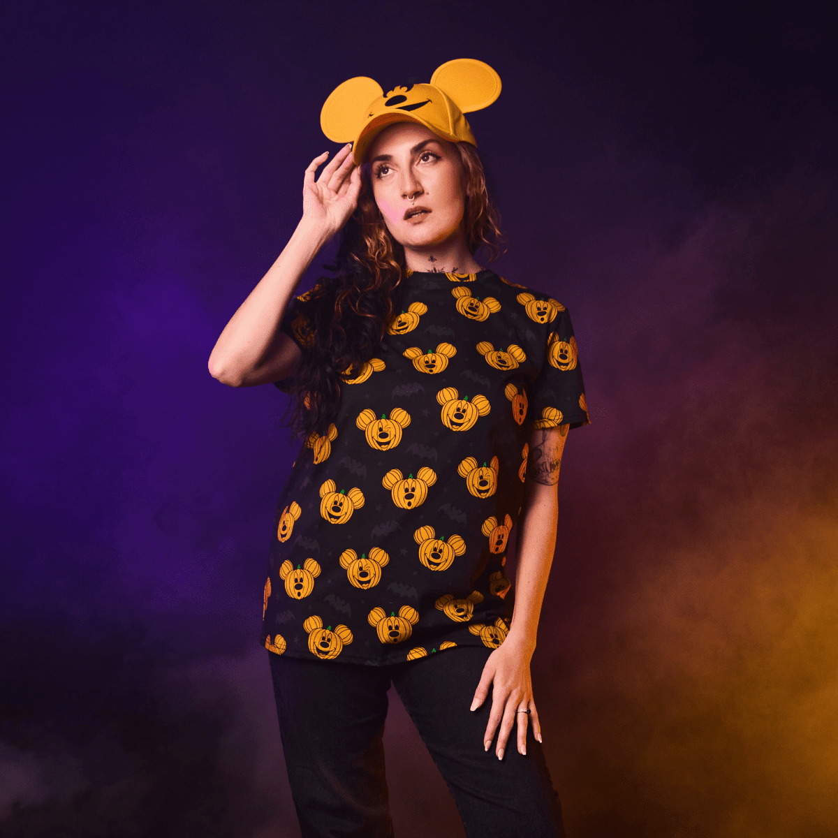 Person wearing a black t-shirt with orange mouse head patterns and a matching hat against a purple background