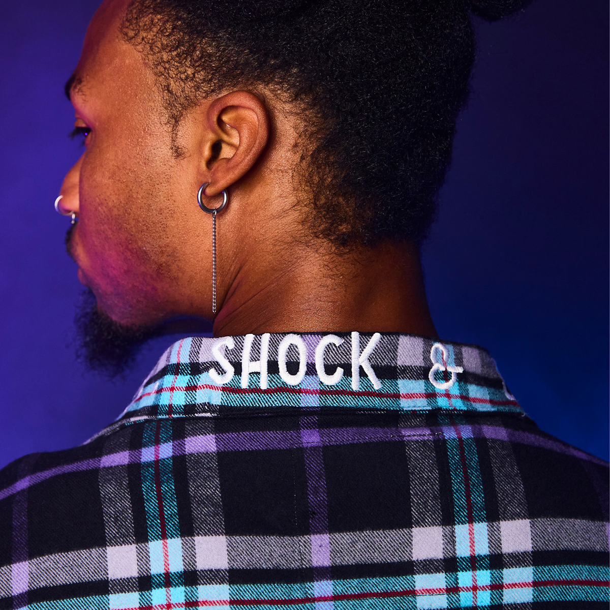 Person wearing a plaid shirt with 'SHOCK & CO' branding on a purple background
