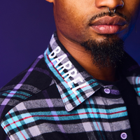 Man wearing a plaid shirt with a brand name on the collar against a dark background