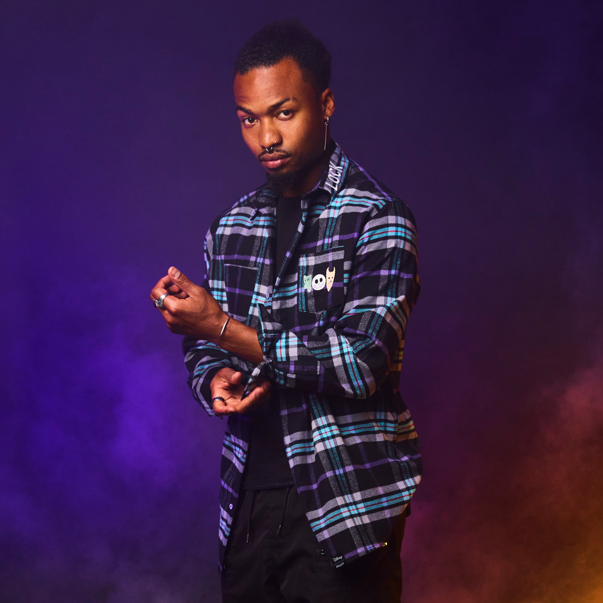 Man wearing a plaid shirt with a brand logo against a purple background