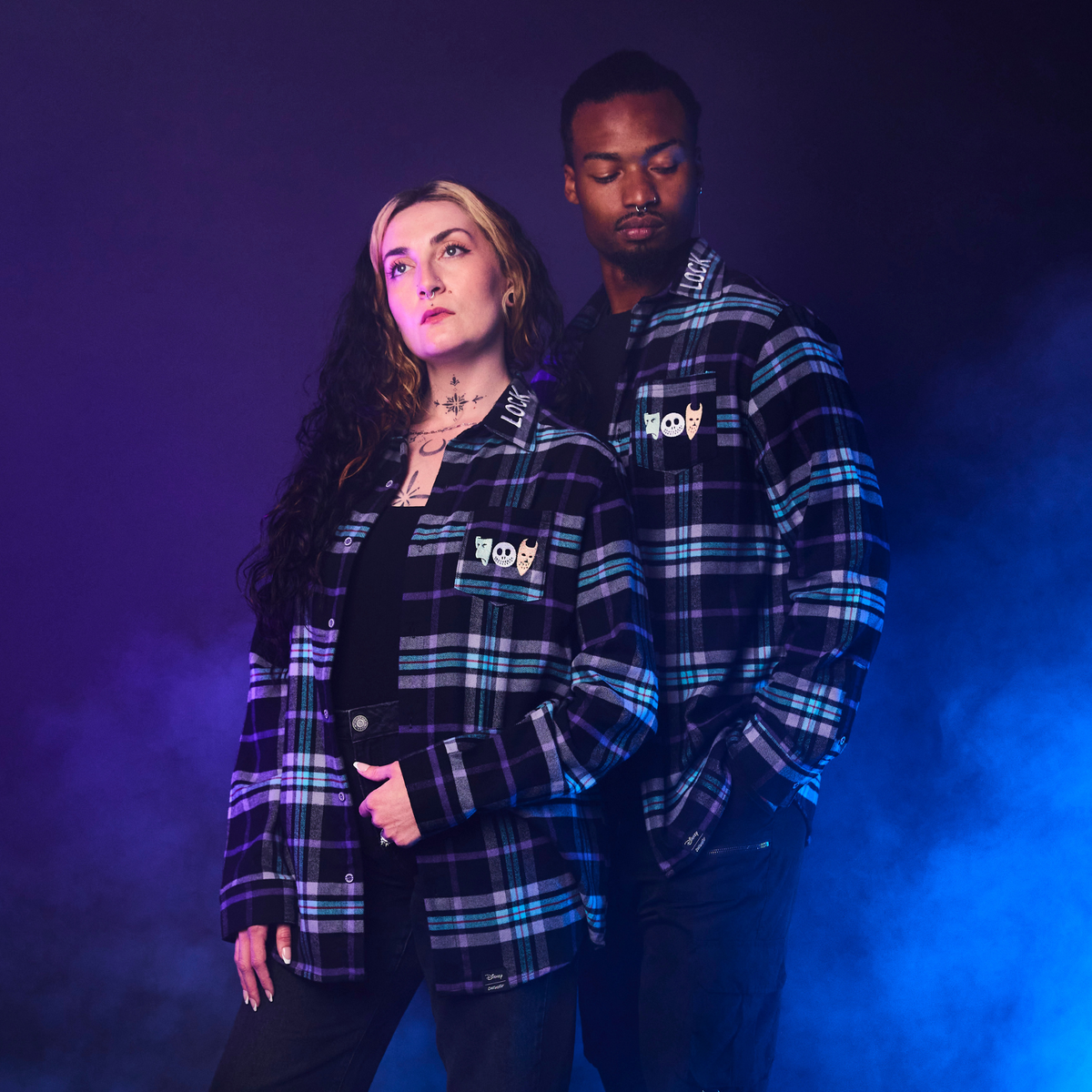 Two people wearing plaid jackets with logos against a dark background