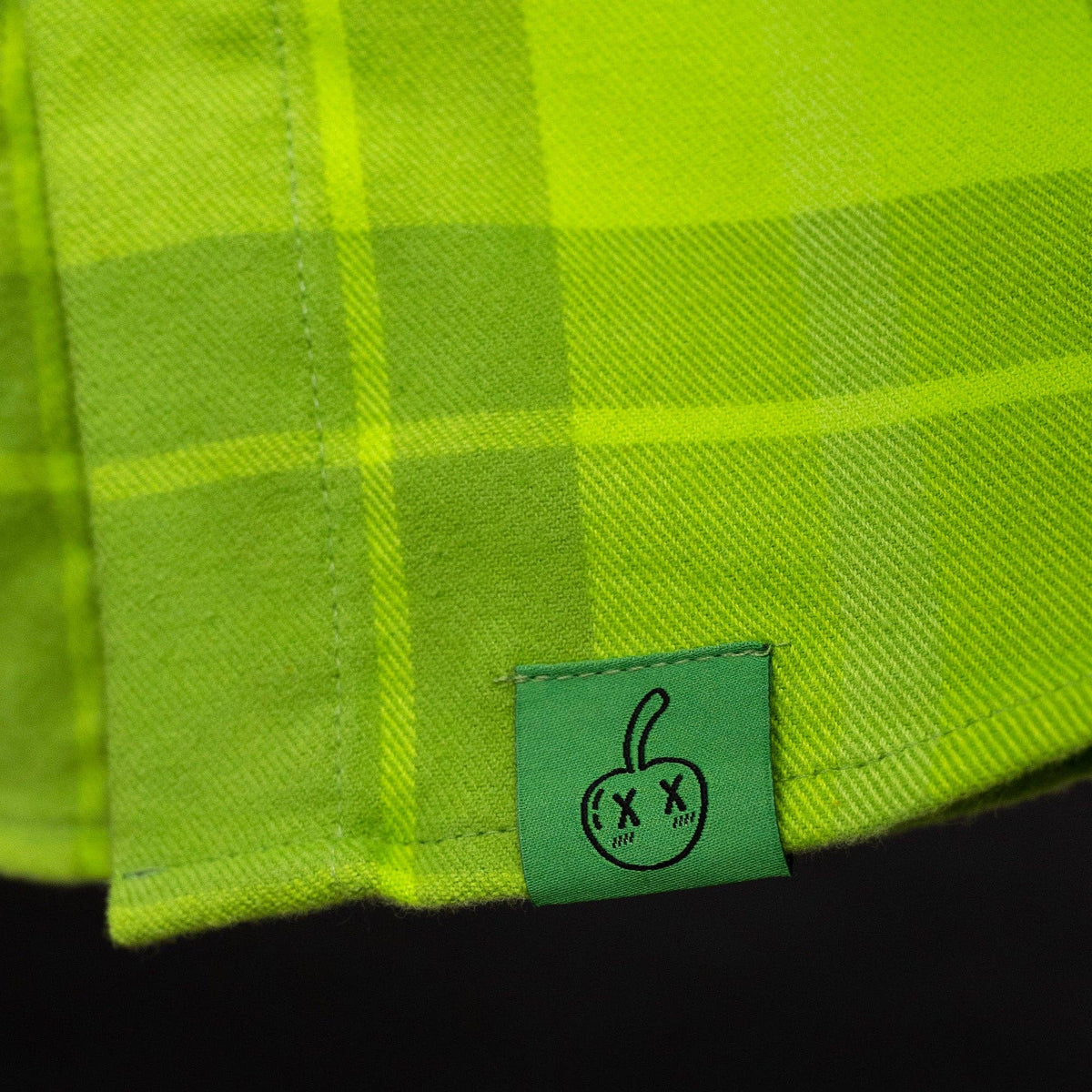 Close-up of a green plaid fabric with a small logo tag on a black background