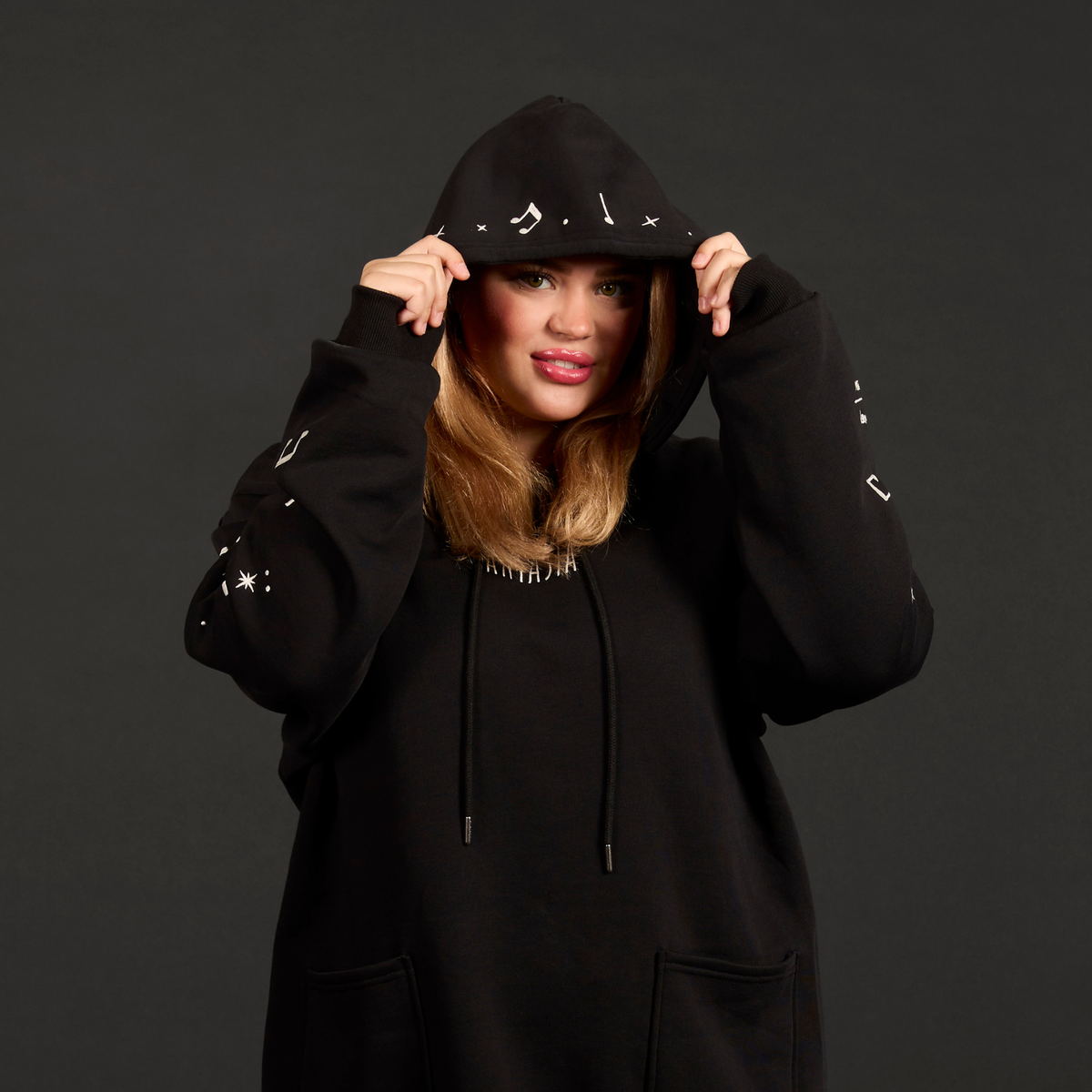 Person wearing a black hoodie with decorative elements on a dark background