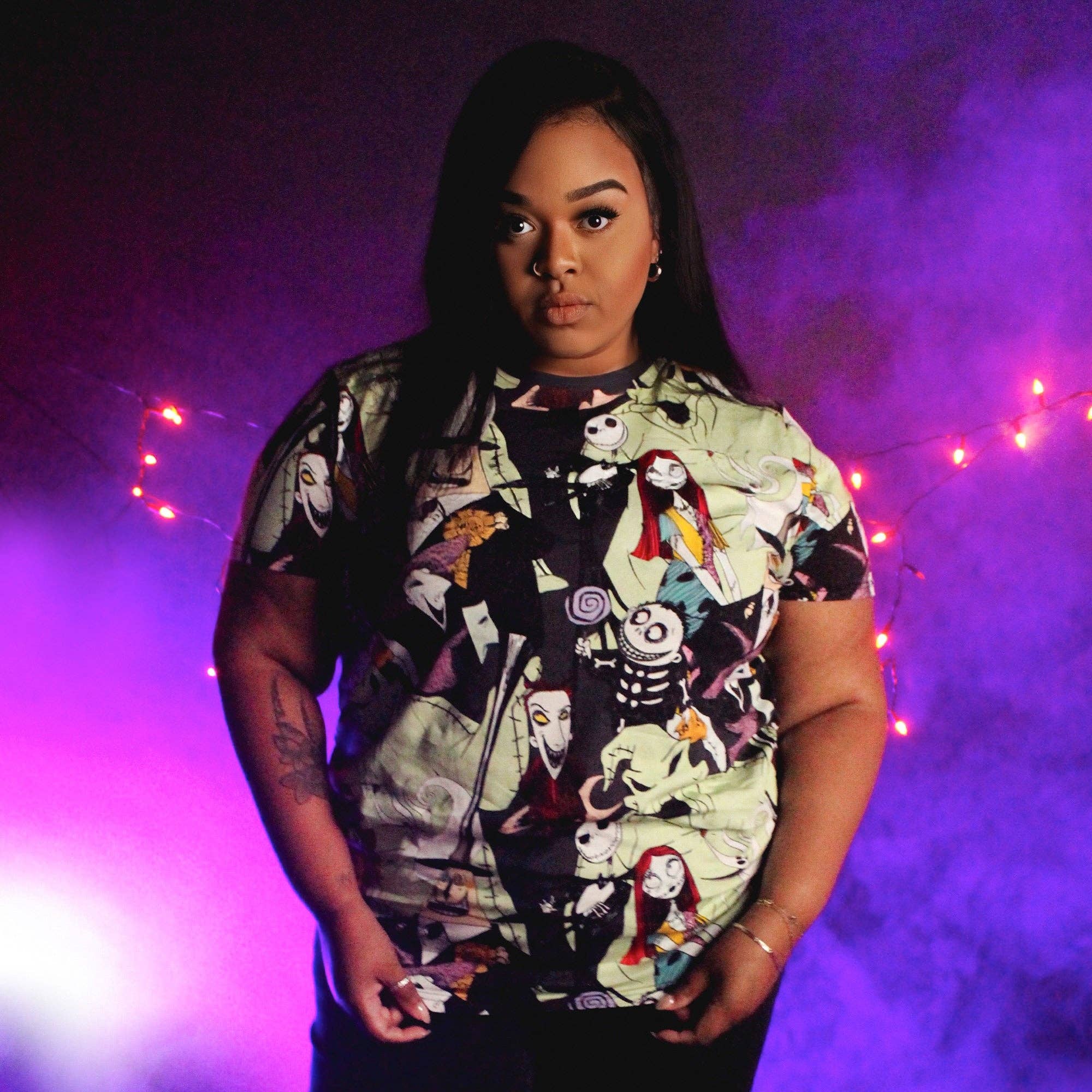 Person wearing a colorful graphic t-shirt against a purple background with string lights.