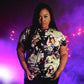 Person wearing a colorful graphic t-shirt against a purple background with string lights.