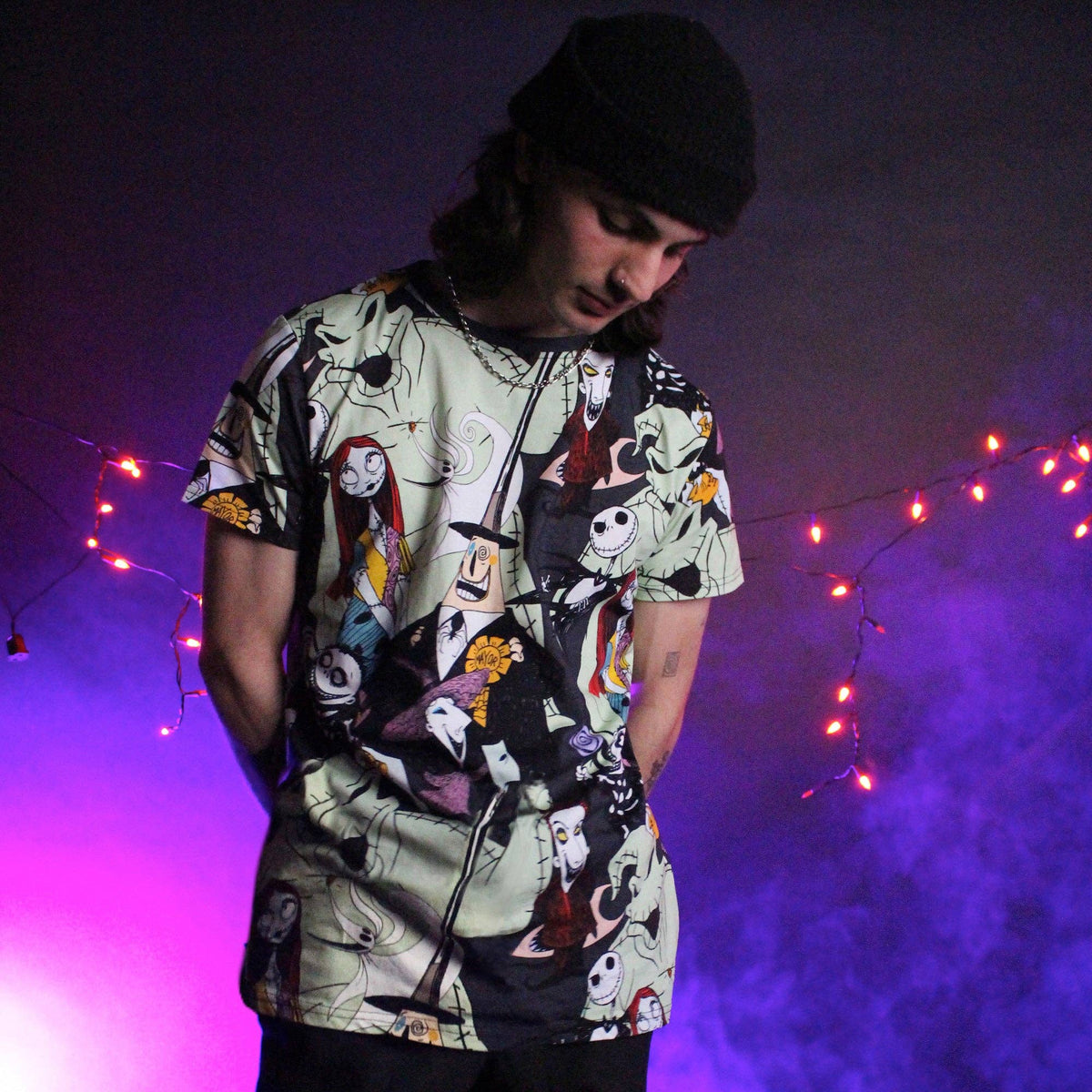 Person wearing a colorful graphic t-shirt with a dark background and string lights.