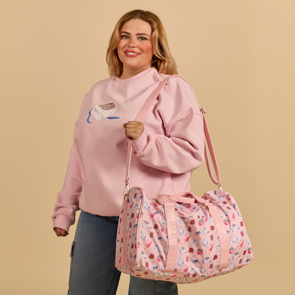 Woman wearing a pink sweatshirt holding a matching pink Cakeworthy Harry Potter Birthday Duffle Bag against a beige background