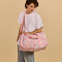 Person holding a pink Cakeworthy Harry Potter Birthday Duffle Bag against a beige background