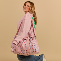 Woman holding a pink Cakeworthy Harry Potter Birthday Duffle Bag against a beige background