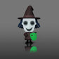 A stylized cartoon figure of a witch holding a glowing green mask, standing on a dark gray reflective surface against a gray gradient background.