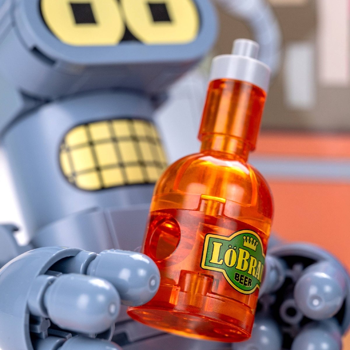 Toy robot holding an orange bottle labeled 'Löbra Beer' with a blurred background