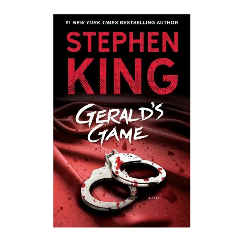 Book cover for Stephen King's 'Gerald's Game' featuring a black background, large red author name, white title text, and a pair of handcuffs with red blood splatter on a red draped surface.