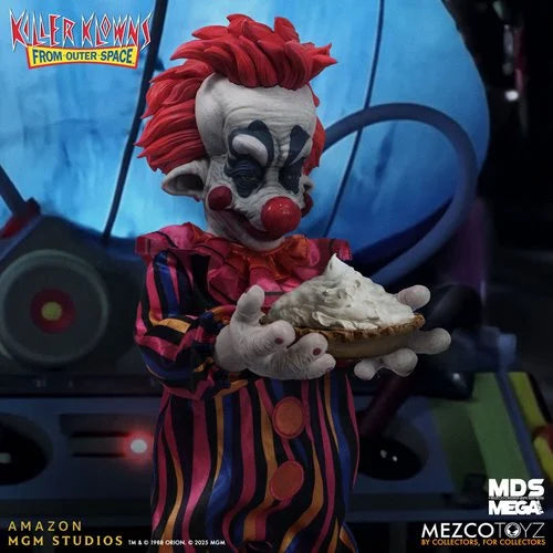 A detailed collectible figure of the Killer Klowns from Outer Space character, holding a large pie. The figure features red hair, a white face with black and red makeup, and a colorful vertically striped suit.