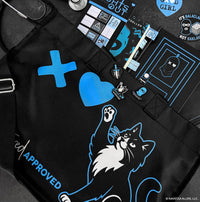 Black apron with blue and white graphics and text, including a cat illustration, on a black surface.