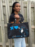 Person holding a black tote bag with a cat design and text outdoors.