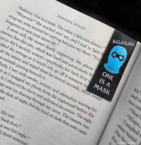 Book with a bookmark featuring a blue mask and text 'One is a Mask' on an open book.