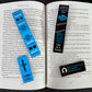Open book with various bookmarks and stickers on a dark surface