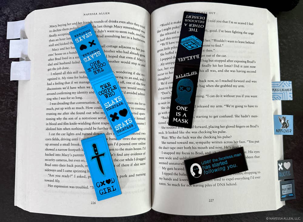 Open book with various bookmarks and stickers on a dark surface