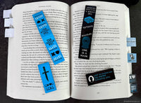 Open book with various bookmarks and stickers on a dark surface