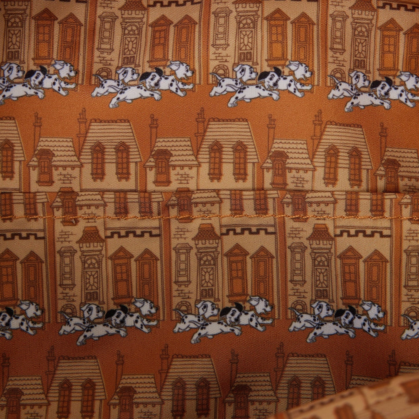 Close-up of a printed fabric featuring repeating illustrations of brown and beige houses with white and black Dalmatian dogs running across an orange-brown background.