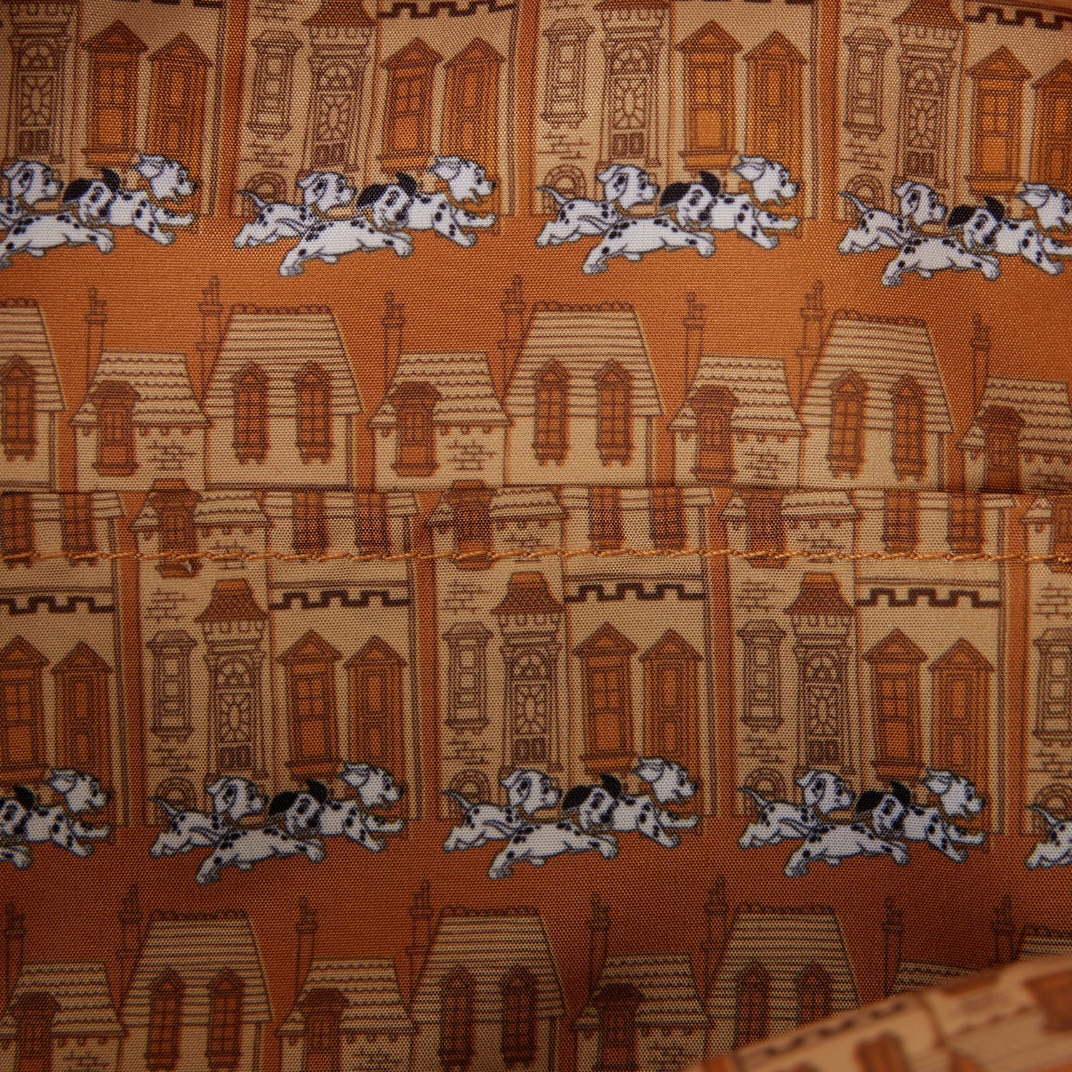 Close-up of a printed fabric featuring repeating illustrations of brown and beige houses with white and black Dalmatian dogs running across an orange-brown background.