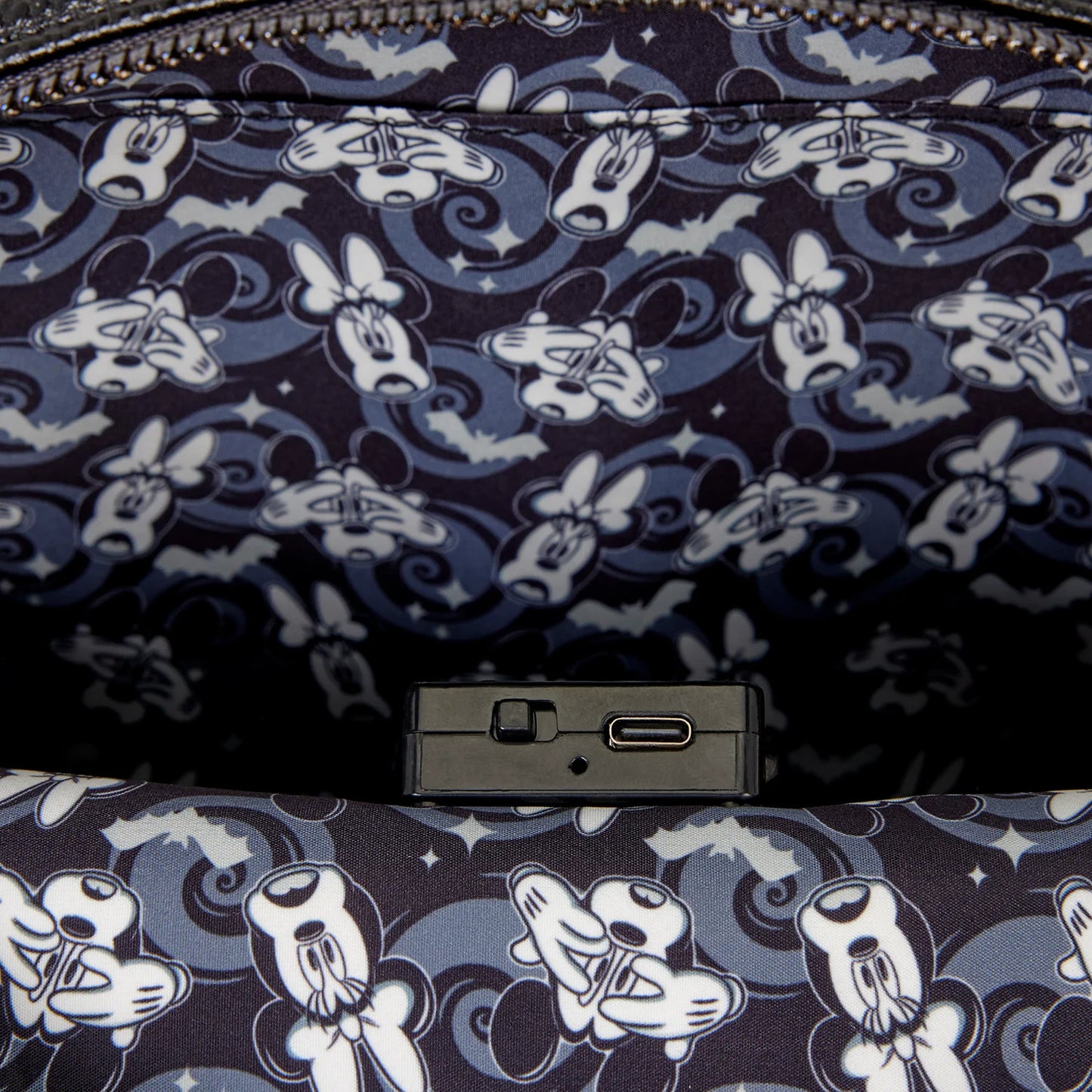 Close-up of a patterned fabric interior with repeating cartoon mouse faces in white and light blue on a dark navy background, plus a small black rectangular hardware piece and zipper visible at the top.