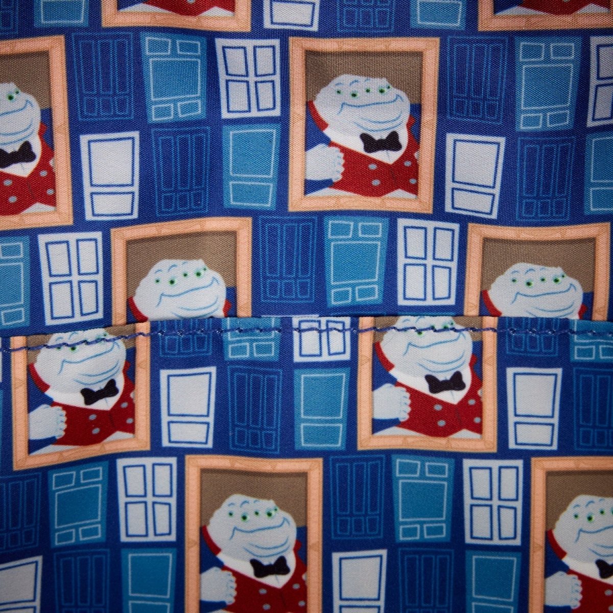 A close-up of patterned fabric featuring a repeating design of a cartoon character in a red outfit framed by blue door motifs on a dark blue background.