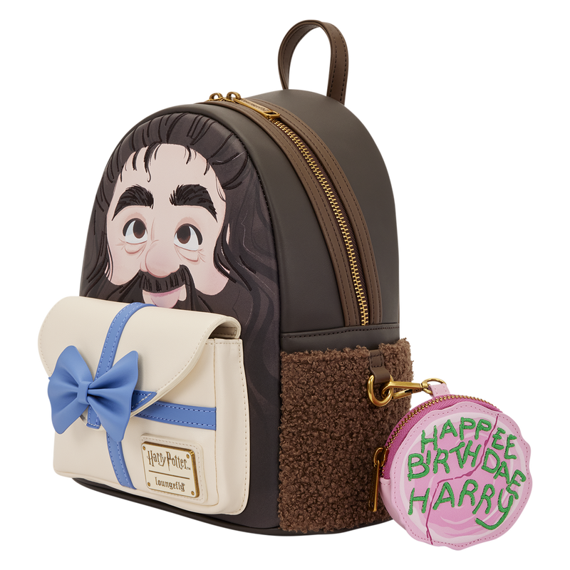 A small dark brown and cream backpack with a printed cartoon face on the front, a blue bow detail on the front pocket, and a round pink coin purse attached with gold hardware. The coin purse reads 'HAPPEN BIRTHDAY HARRY.