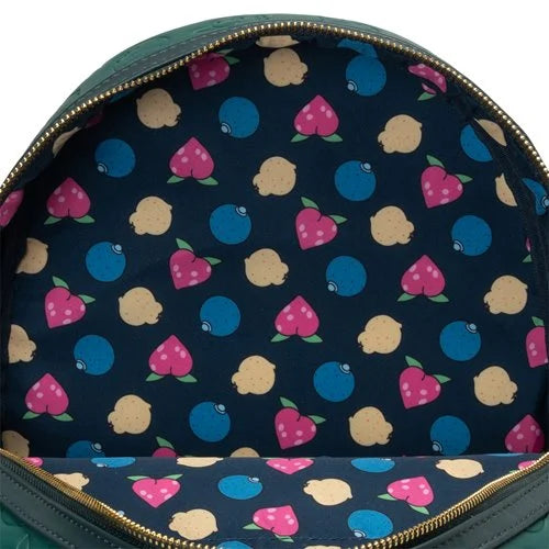Close-up of the interior of a green backpack showing a navy blue fabric lining with a colorful pattern of pink strawberries, blue blueberries, and beige lemons, finished with gold-tone zippers.