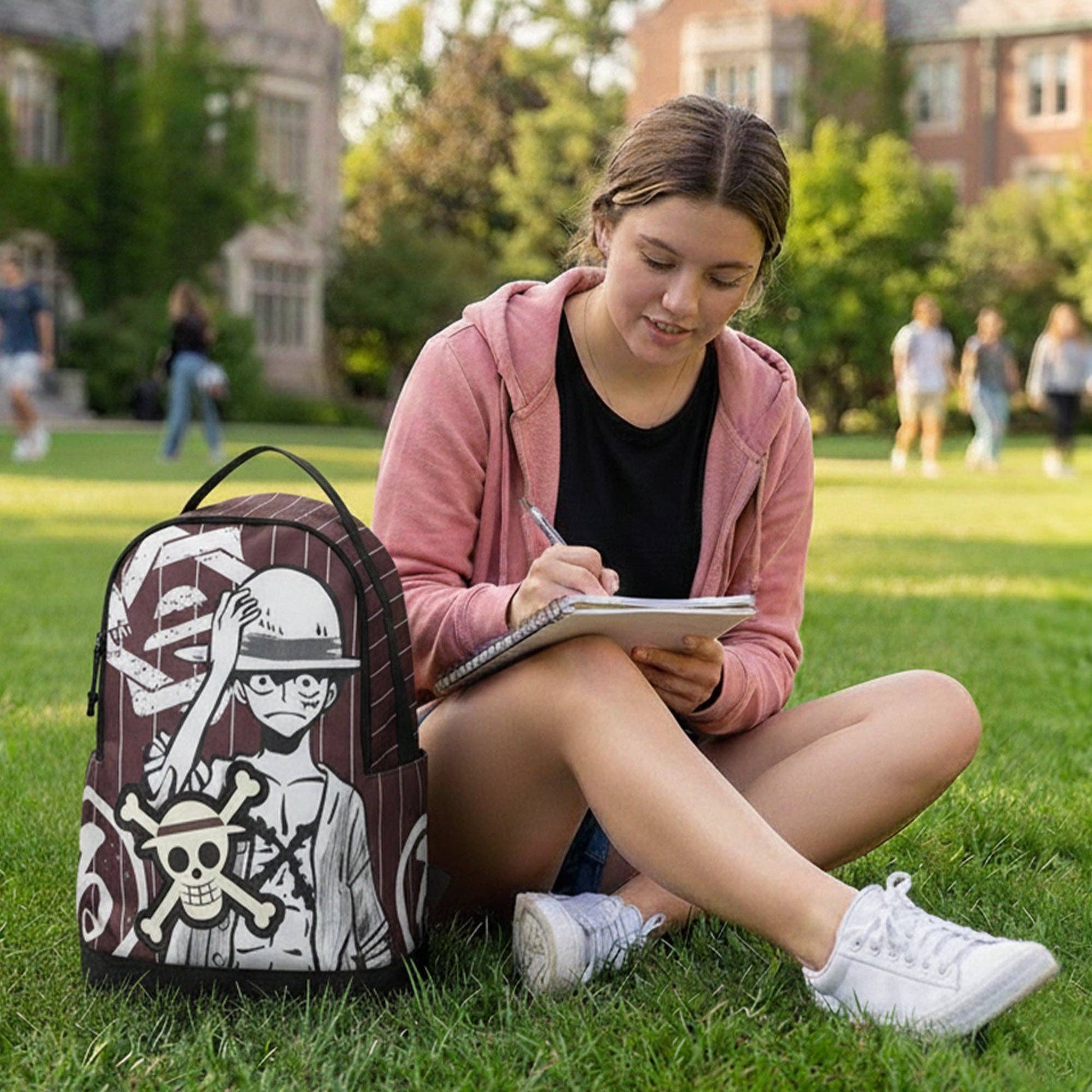 Person sitting on grass with a backpack and notebook, with a building and trees in the background