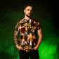Man wearing a ParaNorman All Over Print T-Shirt with graphic designs against a green background
