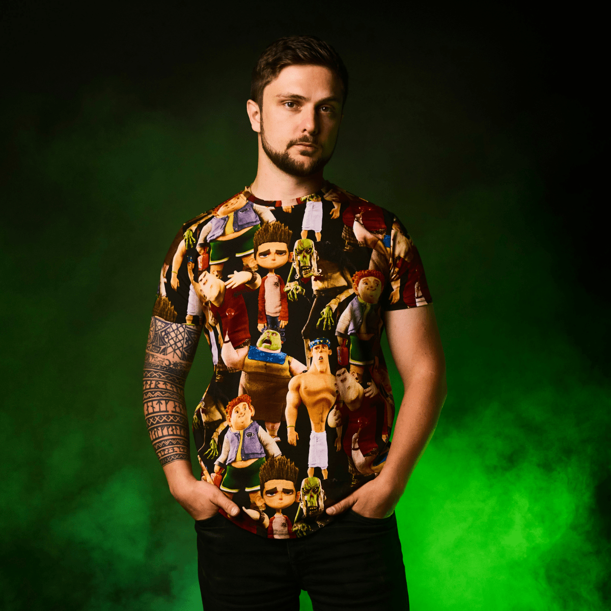 Man wearing a ParaNorman All Over Print T-Shirt with graphic designs against a green background