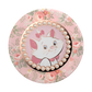 A round pink pop socket featuring a floral pattern with a central illustration of Marie the cat framed by a border of faux pearls.