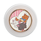 A round white cosmetic compact or container with a gold-toned inner rim and a colorful illustration of three sleeping cats on the front. The cats are in a pink-striped room, with one orange cat wearing a blue bow tie and one dark gray cat wearing a red bow tie.