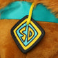 Plush toy with a blue ribbon and a logo patch on a brown background