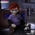 Toy figure of a character with red hair and purple shirt sitting on the floor next to a cardboard box.