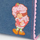 Flat lay of Whatever Makes You Happy Strawberry Shortcake denim tote against a white background