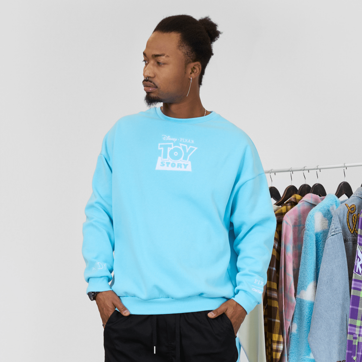 Person wearing a light blue 'Toy Story' sweatshirt in front of a clothing rack.