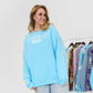 Woman wearing a light blue sweatshirt with a logo, standing next to a rack of clothes.