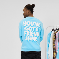 Person wearing a light blue sweatshirt with text on the back, standing in front of a rack of clothes.