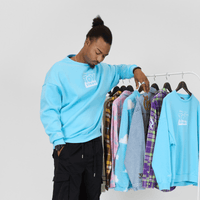Man wearing a light blue sweatshirt with text, standing next to a rack of colorful sweaters.