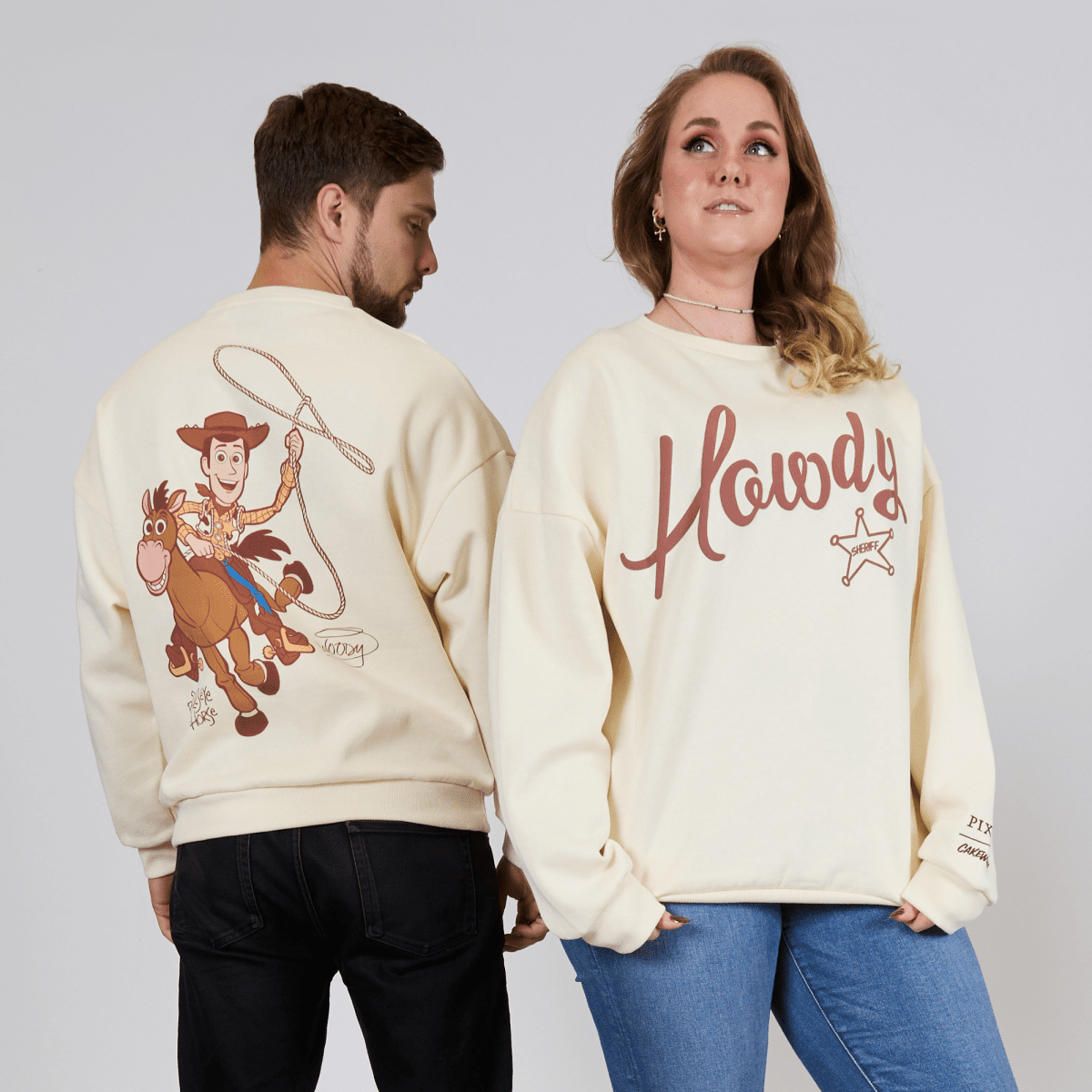 Two people wearing cream-colored sweatshirts with cartoon character and 'Howdy' design.