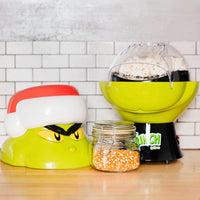Popcorn maker with a Santa hat, jar of popcorn kernels, and a bowl of popped popcorn on a kitchen counter.