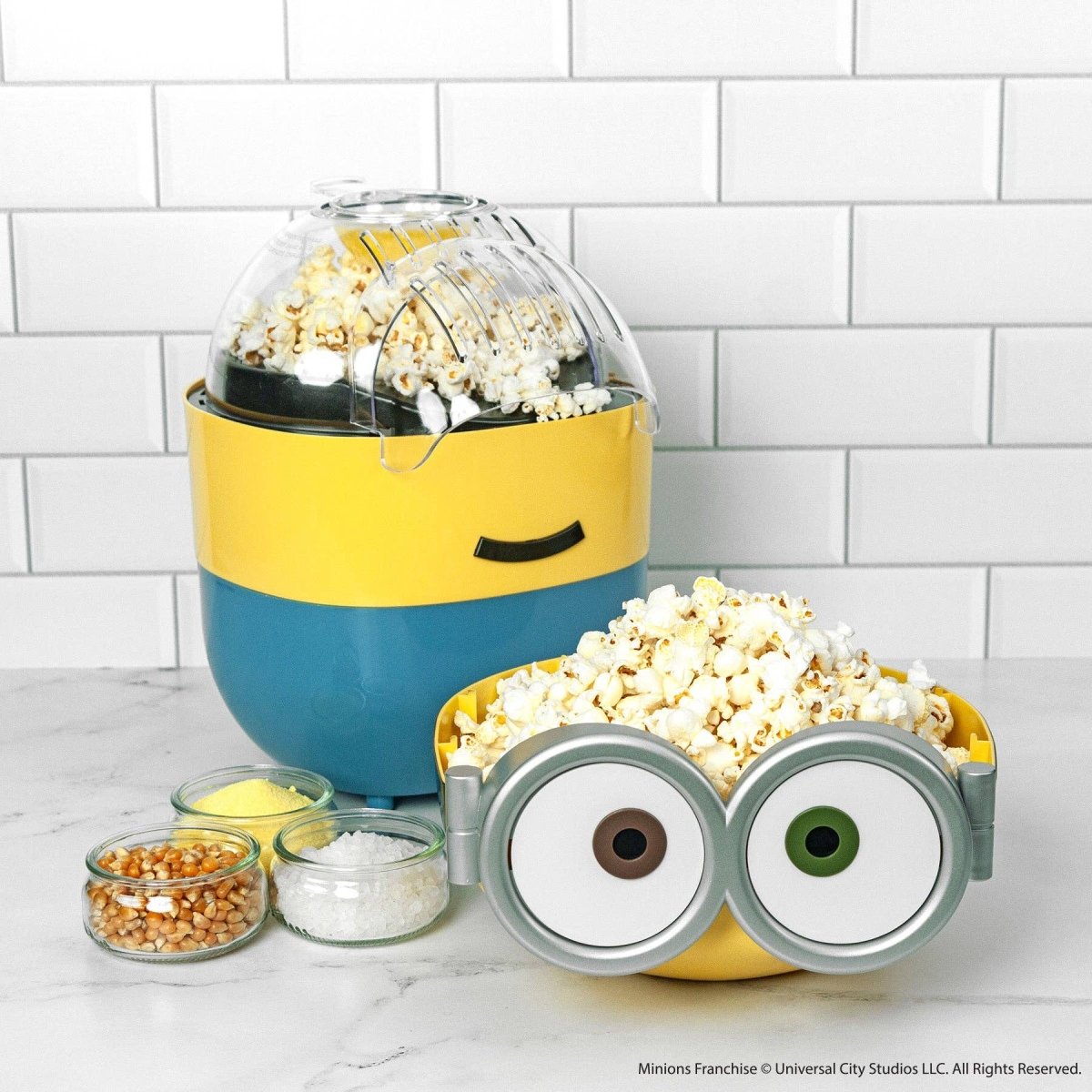 Minion-themed popcorn maker with popped popcorn on a white tiled background
